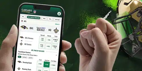 Close-up of a hand holding a smartphone displaying the Caesars Sportsbook app. The app shows NFL betting options, including team matchups, spread, moneyline, and total points, as well as a 'Touchdown Scorers' parlay builder.